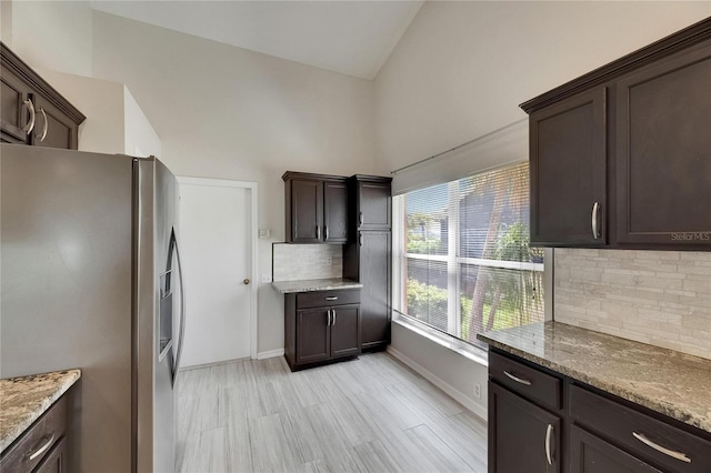 318 Lookout Dr, Apollo Beach, FL 33572 - kitchen featuring stainless steel fridge with ice dispenser, dark brown cabinetry, decorative backsplash, light stone counters, and high vaulted ceiling