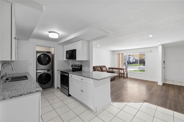 10730 Premier Ave, Port Richey, FL 34668 - kitchen with stainless steel electric stove, stacked washing machine and dryer, black microwave, white cabinets, and recessed lighting