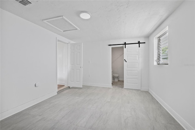 10730 Premier Ave, Port Richey, FL 34668 - unfurnished bedroom with a barn door, attic access, connected bathroom, and a textured ceiling
