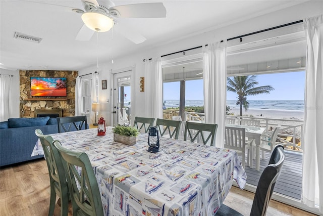 12458 1st St W, Treasure Island, FL 33706 - dining room with light wood finished floors, view of water and beach, a ceiling fan, and a fireplace