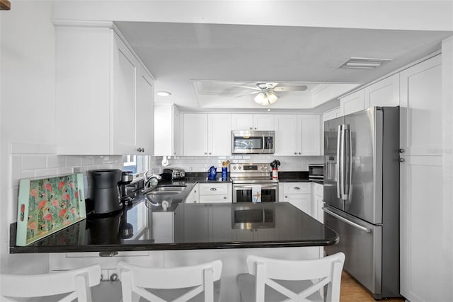 12458 1st St W, Treasure Island, FL 33706 - kitchen with stainless steel appliances, a raised ceiling, a peninsula, backsplash, and ceiling fan