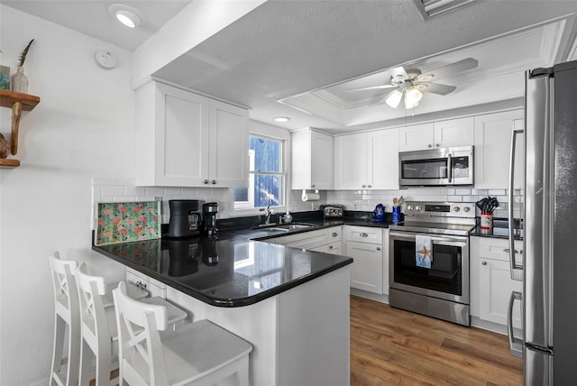 12458 1st St W, Treasure Island, FL 33706 - kitchen with appliances with stainless steel finishes, a peninsula, white cabinetry, tasteful backsplash, and dark countertops