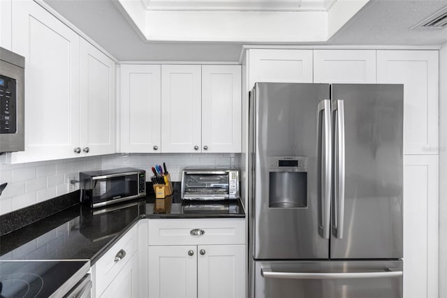 12458 1st St W, Treasure Island, FL 33706 - kitchen with appliances with stainless steel finishes, decorative backsplash, white cabinetry, and dark stone countertops