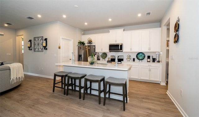 26082 Woven Wicker Bnd, Lutz, FL 33559 - kitchen with appliances with stainless steel finishes, a breakfast bar, white cabinetry, a kitchen island with sink, and recessed lighting