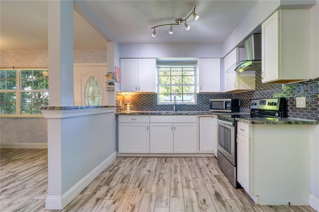 3910 14th Ave N, Saint Petersburg, FL 33713 - kitchen with stainless steel appliances, wall chimney range hood, light wood-style flooring, dark stone countertops, and white cabinets