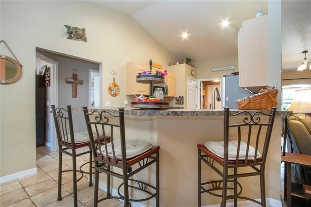 408 River Bed Ct, Wimauma, FL 33598 - kitchen with stainless steel appliances, lofted ceiling, a breakfast bar, a peninsula, and light tile patterned floors