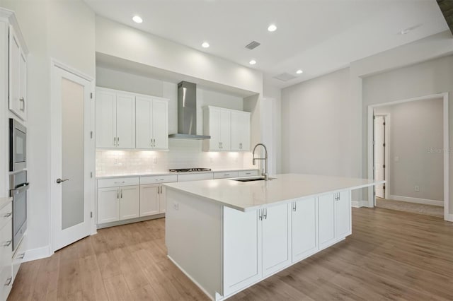14531 Swiss Bridge Dr, Lithia, FL 33547 - kitchen featuring wall chimney range hood, light wood-style floors, tasteful backsplash, a kitchen island with sink, and white cabinetry