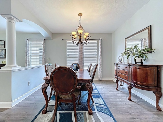 4116 Knollpoint Dr, Wesley Chapel, FL 33544 - dining room featuring ornate columns, a chandelier, arched walkways, wood finished floors, and a textured ceiling