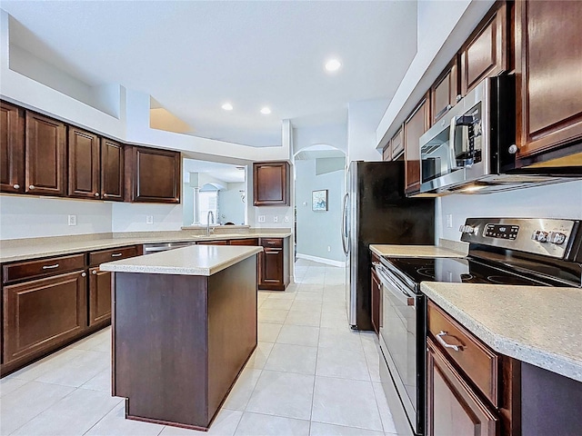 4116 Knollpoint Dr, Wesley Chapel, FL 33544 - kitchen featuring stainless steel appliances, arched walkways, dark brown cabinetry, light tile patterned floors, and recessed lighting