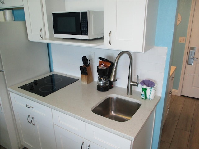 9980 Gulf Blvd Unit 408, Treasure Island, FL 33706 - kitchen featuring white microwave, black electric cooktop, decorative backsplash, white cabinets, and light stone counters