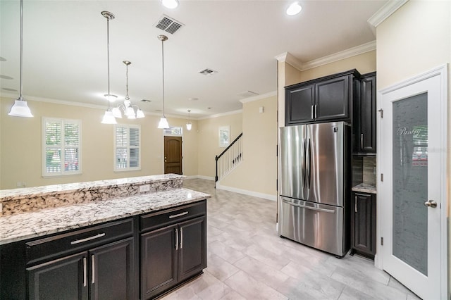 9349 Mira Valle Ln, Winter Garden, FL 34787 - kitchen with freestanding refrigerator, dark cabinetry, decorative light fixtures, light stone counters, and ornamental molding