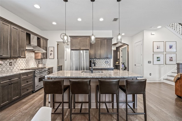 311 12th Ave N, Saint Petersburg, FL 33701 - kitchen featuring high quality appliances, wall chimney range hood, dark brown cabinets, backsplash, and dark wood-style floors