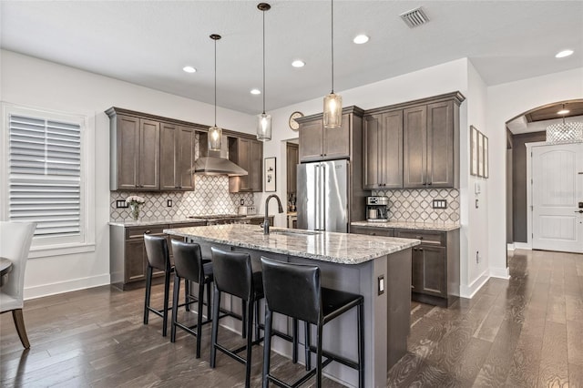 311 12th Ave N, Saint Petersburg, FL 33701 - kitchen with high end refrigerator, wall chimney range hood, arched walkways, dark brown cabinets, and dark wood finished floors