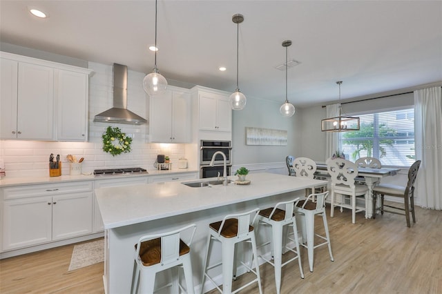 314 Blackrock Ln, Apollo Beach, FL 33572 - kitchen featuring wall chimney exhaust hood, light countertops, a center island with sink, white cabinetry, and appliances with stainless steel finishes