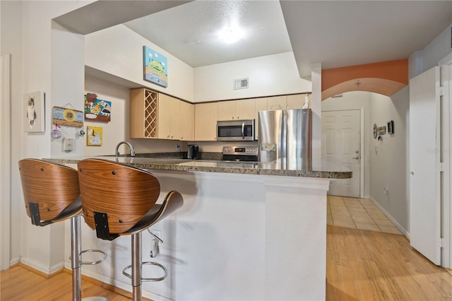 100 4th Ave S Unit 103, Saint Petersburg, FL 33701 - kitchen with appliances with stainless steel finishes, a peninsula, a kitchen breakfast bar, dark countertops, and light wood-style floors