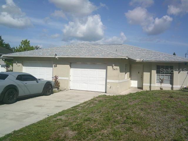 2429/2431 Quentin Ave S, Lehigh Acres, FL 33973 - view of side of home with stucco siding, driveway, an attached garage, roof with shingles, and a lawn