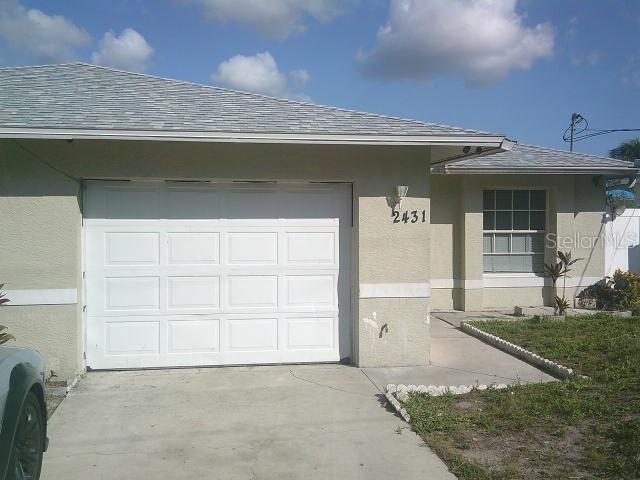2429/2431 Quentin Ave S, Lehigh Acres, FL 33973 - doorway to property featuring stucco siding, roof with shingles, and an attached garage