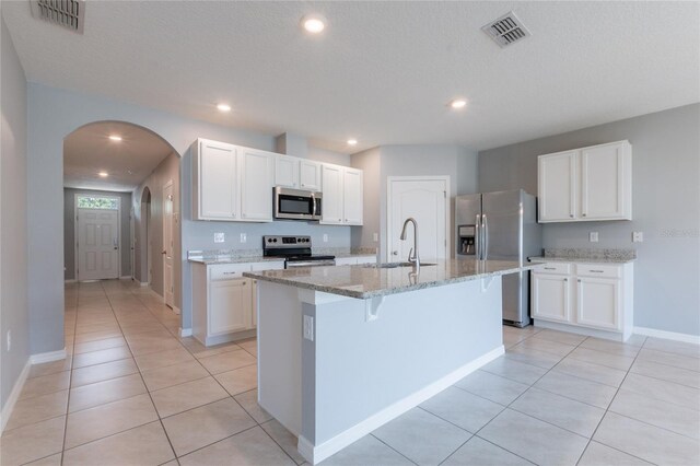 3079 Bethpage Loop, Mount Dora, FL 32757 - kitchen featuring stainless steel appliances, arched walkways, a center island with sink, light stone countertops, and white cabinetry