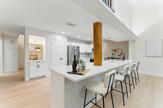 2272 Adam Ct, Palm Harbor, FL 34683 - kitchen with freestanding refrigerator, white cabinetry, light wood-type flooring, a breakfast bar area, and light countertops
