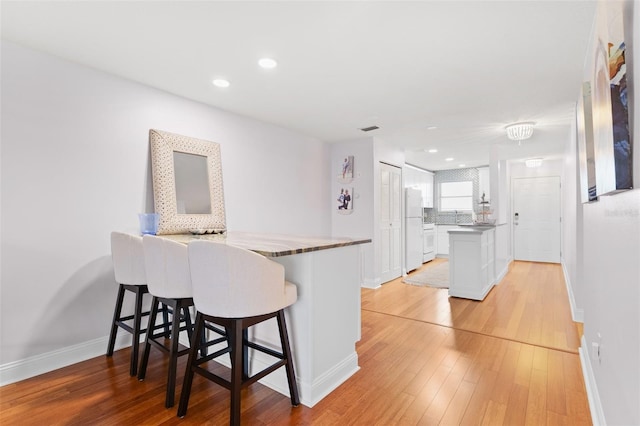 3018 59th St S Unit 405, Gulfport, FL 33707 - kitchen with freestanding refrigerator, white cabinets, a peninsula, light wood-type flooring, and a breakfast bar