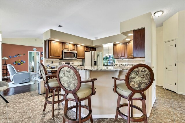 10721 N Ocean Dr, Dunnellon, FL 34434 - kitchen with stainless steel appliances, tasteful backsplash, a breakfast bar, a peninsula, and brown cabinets