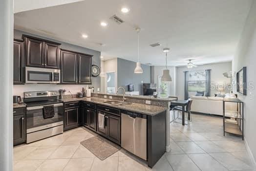 28504 Tranquil Lake Cir, Wesley Chapel, FL 33543 - kitchen featuring appliances with stainless steel finishes, light tile patterned flooring, open floor plan, stone counters, and recessed lighting