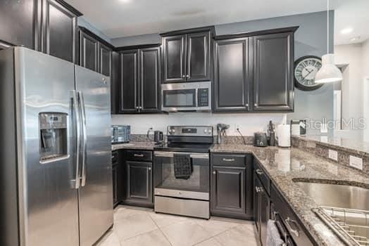 28504 Tranquil Lake Cir, Wesley Chapel, FL 33543 - kitchen featuring stainless steel appliances, stone countertops, dark cabinetry, recessed lighting, and light tile patterned flooring