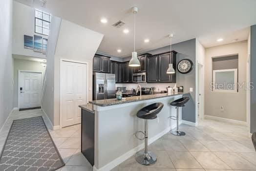 28504 Tranquil Lake Cir, Wesley Chapel, FL 33543 - kitchen with appliances with stainless steel finishes, light tile patterned floors, a kitchen bar, a peninsula, and hanging light fixtures