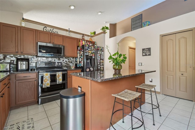 31244 Baclan Dr, Wesley Chapel, FL 33545 - kitchen with stainless steel appliances, a kitchen bar, light tile patterned flooring, tasteful backsplash, and arched walkways