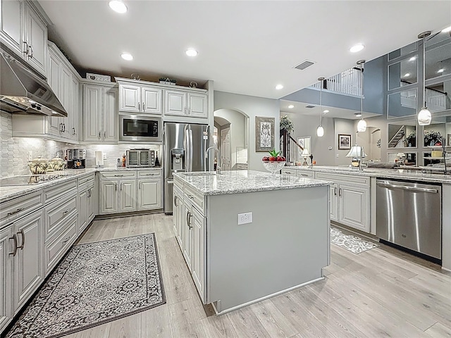 33668 Willow Point Ct, Wesley Chapel, FL 33545 - kitchen with appliances with stainless steel finishes, arched walkways, under cabinet range hood, an island with sink, and light wood-style flooring