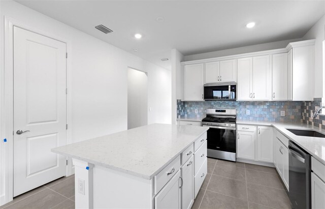 6133 Wire Grass Ct, Nokomis, FL 34275 - kitchen featuring stainless steel appliances, light tile patterned floors, a center island, decorative backsplash, and light stone counters