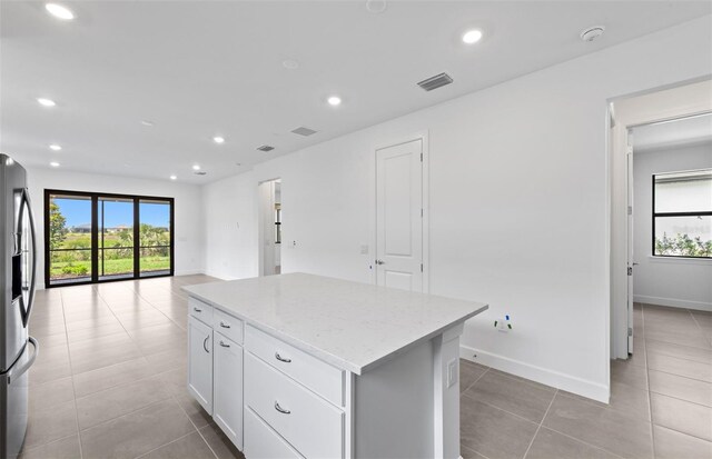 6133 Wire Grass Ct, Nokomis, FL 34275 - kitchen with stainless steel fridge, a kitchen island, light tile patterned floors, light stone countertops, and healthy amount of natural light
