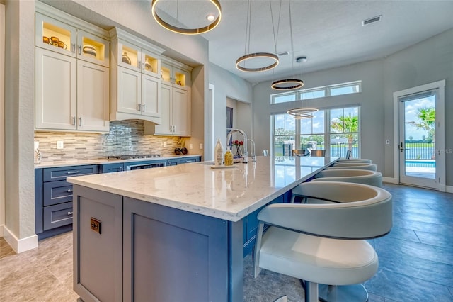 12902 SW 138th Loop, Dunnellon, FL 34432 - kitchen with a kitchen island with sink, decorative backsplash, glass insert cabinets, light stone counters, and a breakfast bar area