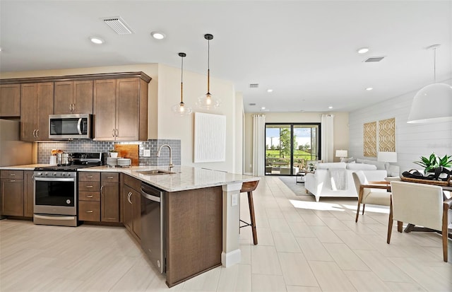 14317 Eagle Branch Dr, Nokomis, FL 34275 - kitchen featuring stainless steel appliances, light stone countertops, a peninsula, tasteful backsplash, and decorative light fixtures