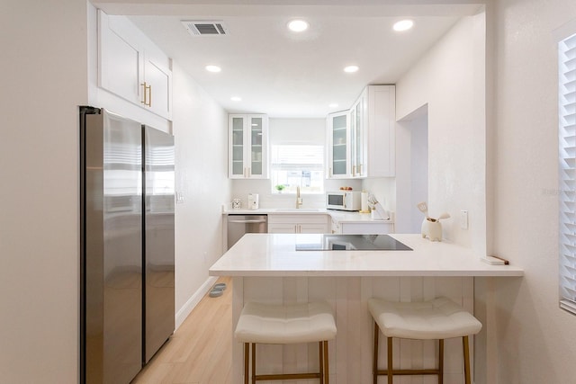 434 77th Ave, St Pete Beach, FL 33706 - kitchen with appliances with stainless steel finishes, a kitchen bar, white cabinets, glass insert cabinets, and recessed lighting