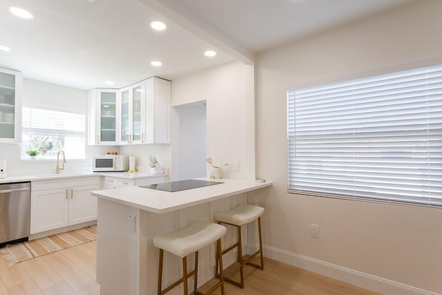 434 77th Ave, St Pete Beach, FL 33706 - kitchen featuring stainless steel dishwasher, black electric stovetop, white microwave, light wood-style floors, and a kitchen breakfast bar