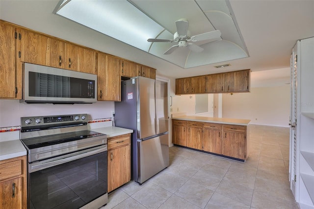 2609 Lancaster Dr, Sun City Center, FL 33573 - kitchen with appliances with stainless steel finishes, a peninsula, brown cabinetry, and a ceiling fan