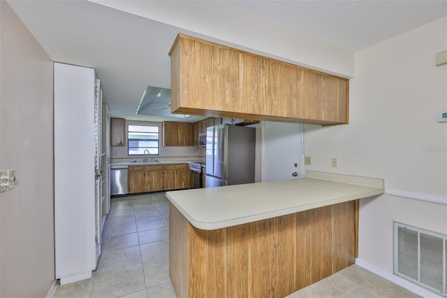 2609 Lancaster Dr, Sun City Center, FL 33573 - kitchen featuring stainless steel appliances, a peninsula, light countertops, light tile patterned flooring, and brown cabinets