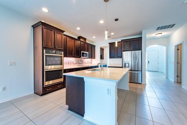 11035 Sage Canyon Dr, Riverview, FL 33578 - kitchen featuring stainless steel appliances, decorative backsplash, a kitchen island with sink, light tile patterned floors, and light countertops