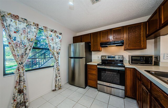 1729 Seascape Cir Unit 102, Tarpon Springs, FL 34689 - kitchen featuring appliances with stainless steel finishes, under cabinet range hood, light countertops, a textured ceiling, and light tile patterned floors