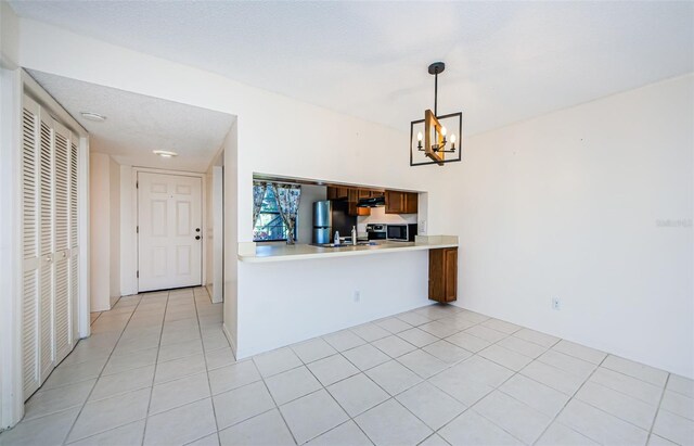 1729 Seascape Cir Unit 102, Tarpon Springs, FL 34689 - kitchen with stainless steel microwave, a chandelier, light countertops, freestanding refrigerator, and light tile patterned floors