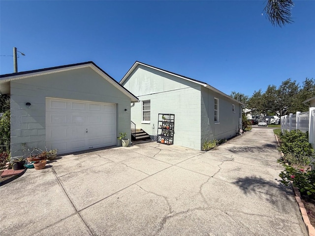 view of property exterior featuring concrete driveway, a detached garage, concrete block siding, and an outdoor structure