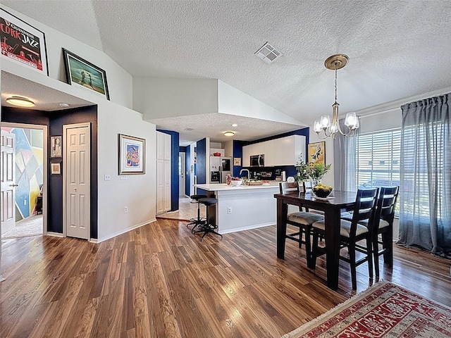 dining area featuring lofted ceiling, wood finished floors, a textured ceiling, and a chandelier