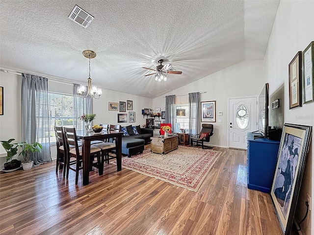 dining room with wood finished floors, a textured ceiling, ceiling fan, vaulted ceiling, and a chandelier