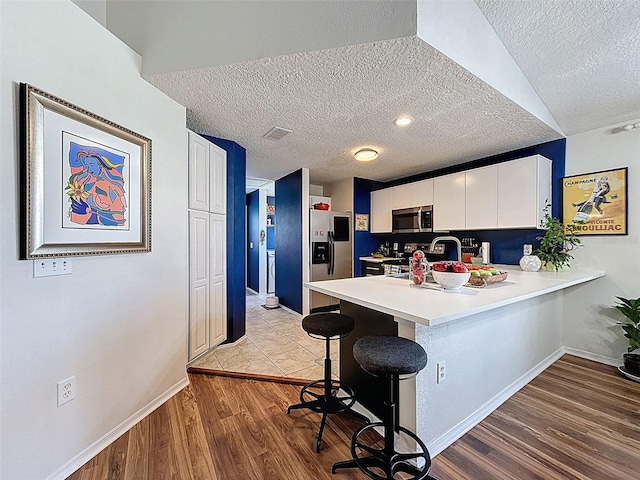 kitchen with stainless steel appliances, a peninsula, a kitchen breakfast bar, a textured ceiling, and light countertops
