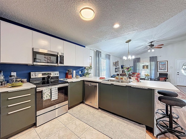 kitchen with stainless steel appliances, a peninsula, a textured ceiling, light countertops, and a chandelier