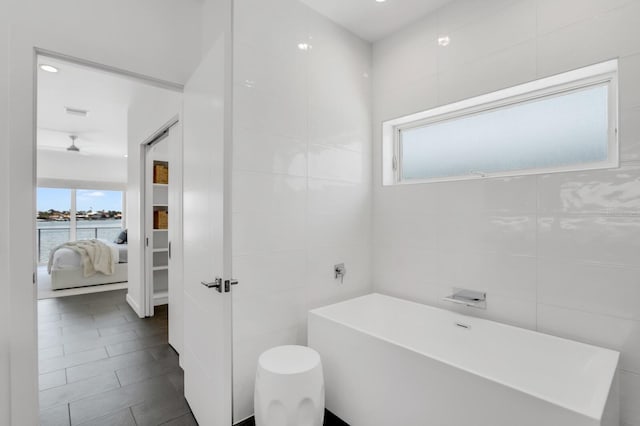 905 Bay Point Dr, Madeira Beach, FL 33708 - ensuite bathroom with a soaking tub, healthy amount of natural light, tile walls, a water view, and tile patterned flooring
