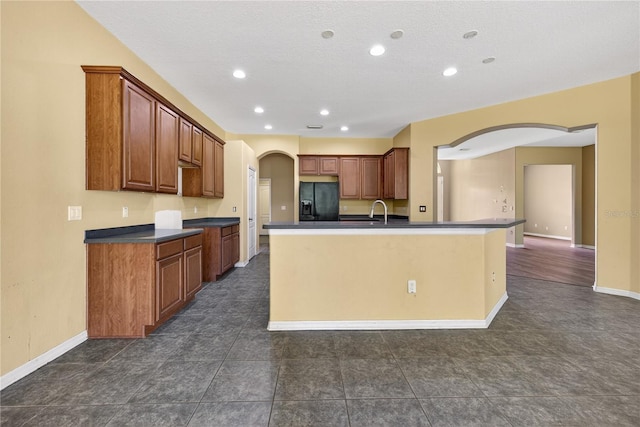 1835 Fircrest Ct, Wesley Chapel, FL 33543 - kitchen with black fridge with ice dispenser, dark countertops, arched walkways, brown cabinetry, and recessed lighting