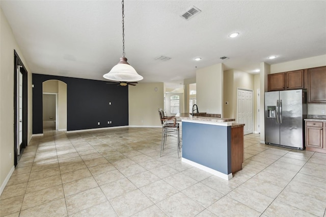 297 Beacon Pointe Dr, Ocoee, FL 34761 - kitchen featuring stainless steel refrigerator with ice dispenser, arched walkways, light tile patterned floors, a kitchen breakfast bar, and light countertops