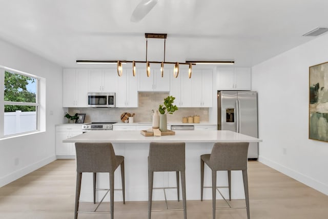 3381 19th Pl SW, Largo, FL 33774 - kitchen featuring stainless steel appliances, a breakfast bar area, light wood-style flooring, a kitchen island, and white cabinetry